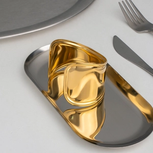 Minimalist wide wave 18K gold plated stainless steel cuff bracelet on a metal tray