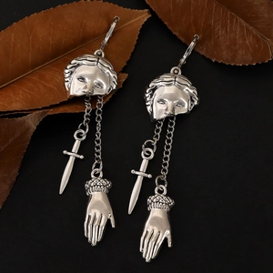 Gothic silver earrings with hand, mask, and dagger charms on a minimalist black background