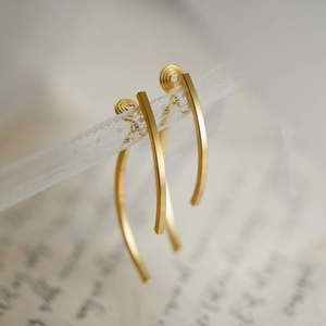 Elegant long gold curved bar clip-on earrings displayed on white lace with a vintage feel