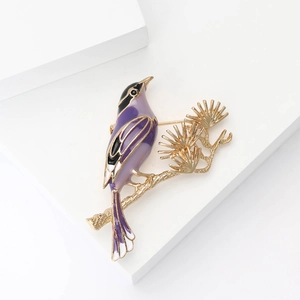 Enamel magpie and pine branch brooch in purple and gold on white background