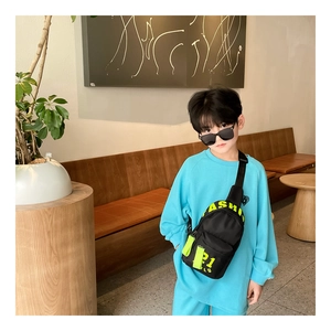 Sac poitrine enfant noir avec imprimé vert néon, porté par un enfant dans un café