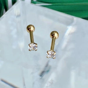 Macro shot of gold four-prong set round zircon stud earrings on a crystal stand