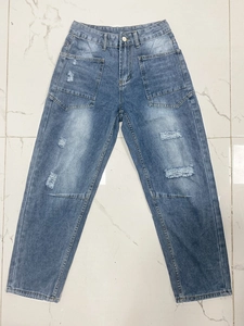 Detail van de blauwe spijkerbroek met grote opgestikte voorzakken en distressed denim look