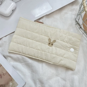 Detail of quilted bunny embroidery and button closure on cream soft storage bag