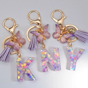 Detail of resin letter keychain with purple glitter, star sequins and leather tassel