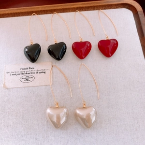 Détail de boucles d'oreilles cœur en perles noir, rouge et crème sur un plateau en bois