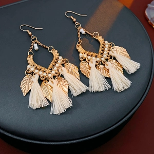 Detail of bohemian gold leaf earrings with white beads and elegant beige tassels