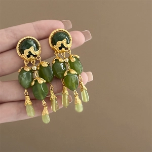 Detail of vintage gold earrings with green jade-like beads and elegant tassel design
