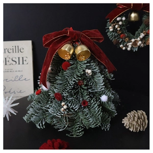Close-up of mini Christmas tree with red velvet bow, gold bell, and festive berries