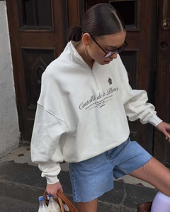 Detail of white half-zip sweatshirt with black logo print on a vintage wood door background