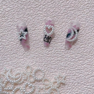 Macro detail of resin pearl heart, star, and moon charms on abstract nail art design