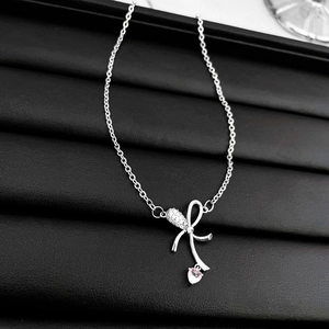 Close-up of silver bow necklace with pink heart zircon on black leather jewelry box
