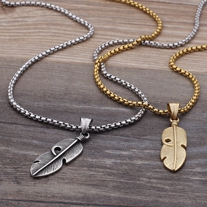 Retro stainless steel feather pendant necklaces in silver and gold on a dark wood background