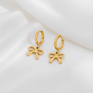 Detailed macro view of gold-plated stainless steel bow drop earrings on white silk fabric