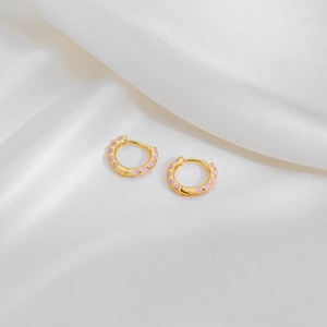 Close-up of gold hoop earrings with pink enamel dots on white silk fabric