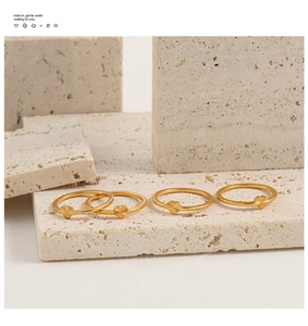 Detailed macro of four golden heart-engraved rings on minimalist beige stone stand