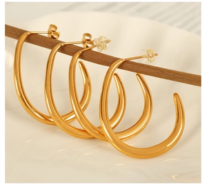 Macro shot of thick gold-plated C-shape earrings hanging on a dark wood bar