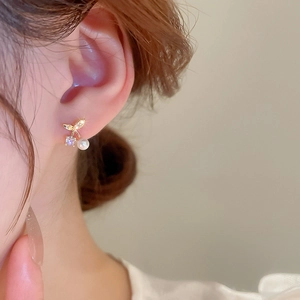 Close-up of cherry design gold stud earrings with pearls and zircons on ear