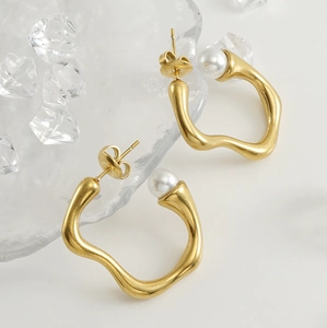 Macro shot of 18K gold irregular wavy earrings with white pearl detail and metallic shine