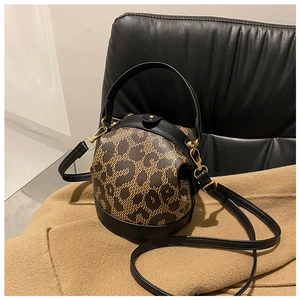 Detail of leopard print knit and black leather bucket bag with gold hardware on camel coat