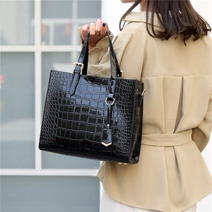 Elegant black crocodile pattern tote bag with gold hardware held by a fashion model