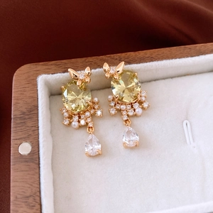 Macro shot of 18k gold butterfly earrings with yellow oval gems and pearl details