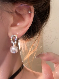 Close-up of elegant horse-bit pearl earring with zircon pave setting on a female model