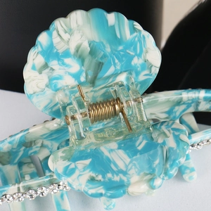 Detail of blue marble acetate hair claw with shell design and shimmering rhinestones