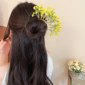 Detailed view of yellow floral hair pin set in a half-up bun on a female model