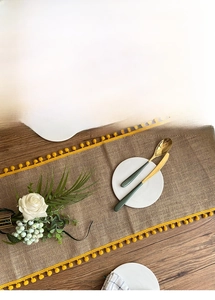 Close-up of natural burlap table runner with yellow pom-pom trim on dark wooden table