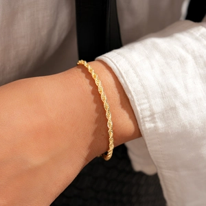 Détail d'un bracelet chaîne corde doré au poignet avec un design en métal poli et torsadé