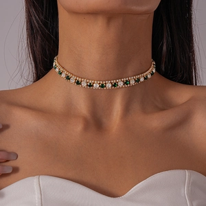 Close-up of gold choker necklace with green and white crystals on female model