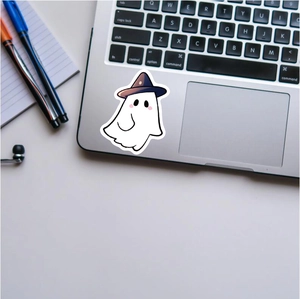 Cute cartoon ghost sticker with purple hat applied on a silver laptop surface