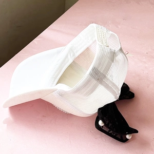 Detail of white mesh baseball cap featuring a black lace bow and white pearl accents
