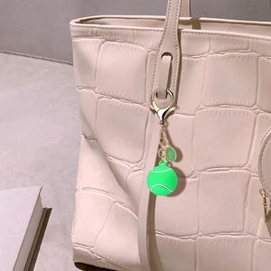 Tennis racket and ball keychain accessory hanging on a stylish beige alligator handbag