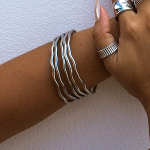 Close-up of wavy polished silver bangles and minimalist metal rings worn by a model