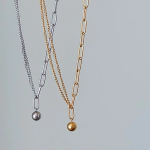 Close-up of asymmetrical mixed chain necklace featuring a polished gold ball pendant