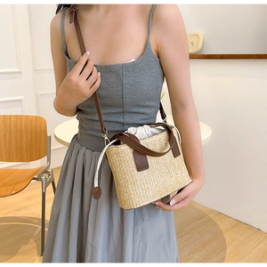 Straw woven bucket bag with brown leather handles and adjustable strap on female model