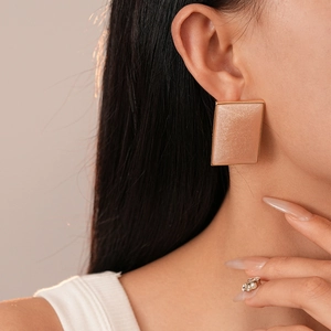 Close-up of model wearing gold-edged champagne rectangular resin earrings in soft light