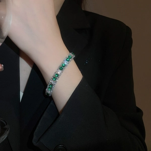 Detailed close-up of a silver tennis bracelet with emerald green and white zircons