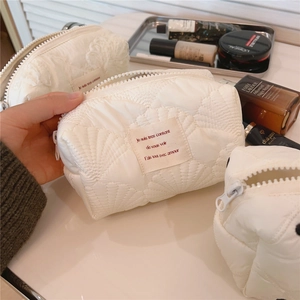 Gros plan d'une trousse de maquillage matelassée crème avec broderie coquillage