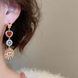 Detailed close-up of a gold Hamsa hand earring with a red heart and evil eye on ear