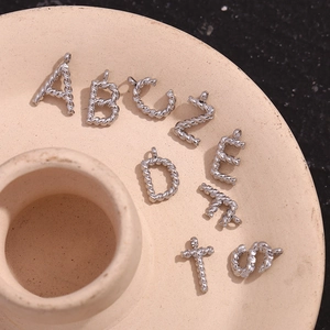 Silver stainless steel mini twisted letter pendants A-Z on a ceramic dish background