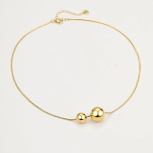 Detail of gold snake chain necklace featuring two polished hollow spherical pendants