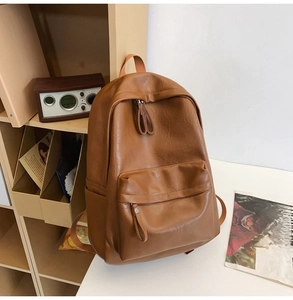 Detailed view of brown leather backpack with front zipper pocket on minimalist desk