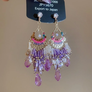 Close-up of gold-tone tassel earrings with purple crystals and sparkling rhinestones