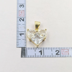 Detailed view of a gold heart pendant with clear zircons next to a measuring tape