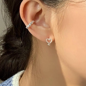 Close-up of silver heart stud and cubic zirconia ear cuff set on model ear