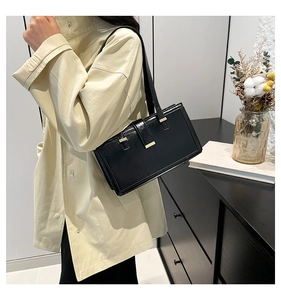 Detail of minimalist black rectangle shoulder bag with gold clasp on beige trench coat