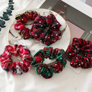 Flat lay of five Christmas flannel scrunchies with red and green plaid and snowflake patterns